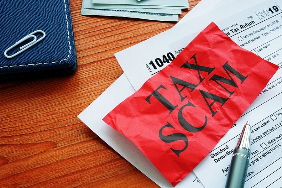 Red tax scam slip placed across a 1040 tax form sitting on a cherry wood desk with a book, money, and pen