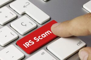 Person pressing a red IRS scam button on a white and grey laptop