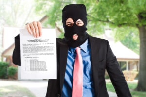 Man in a black ski mask with a black jacket, blue shirt, and pink tie holding a piece of paper with tax information on it