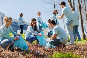 Community in blue shirts with blue plastic bags volunteering to pick up trash on the side of the road