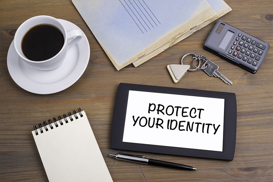 Screen with protect your identity text with papers, a cup of coffee, and a small notebook on a brown wooden table.