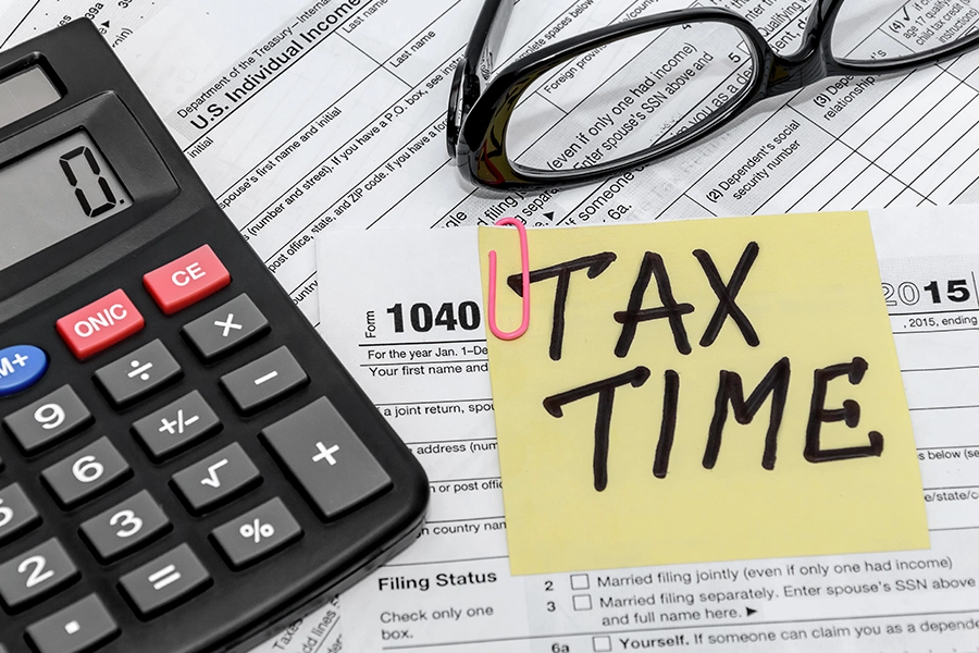 Multiple tax document forms, a calculator, glasses, and a sticky note that reads tax time to indicate that you need a tax filing professional in Springfield, IL.