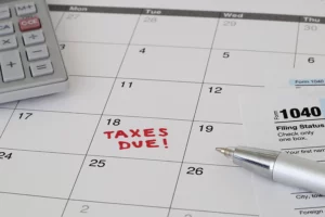 A monthly calendar with the date when taxes are due and several office supplies and tax documents lying on a table in Springfield, IL.