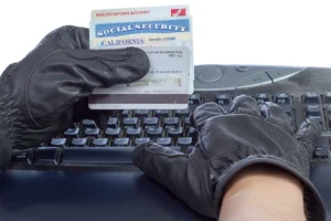 Hands in black gloves holding a credit card, health savings card, and social security card near a keyboard, implying someone is about to commit identity theft in Springfield, IL.