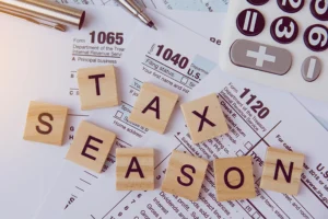 The phrase "tax season" resting atop a stack of tax forms beside a calculator on a desk in the JLW Tax & Bookkeeping office in Springfield, IL.