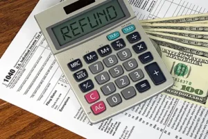 JLW Tax & Bookkeeping—A calculator reads “refund” on the screen and sits on top of tax forms and several hundred-dollar bills, signifying a good tax return.