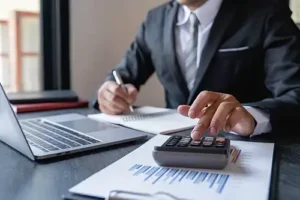 JLW Tax & Bookkeeping Services—A professional tax consultant in Springfield, IL, uses a calculator and computer to check a business’s records and perform a monthly reconciliation.