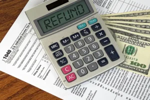 JLW Tax & Bookkeeping—A calculator reads “refund” on the screen and sits on top of tax forms and several hundred-dollar bills, signifying a good tax return.